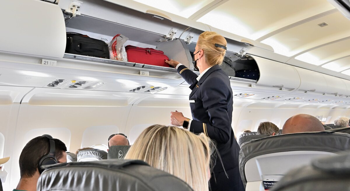 Eine Flugbegleiterin vor einem geöffneten Gepäckfach mit Handgepäck.