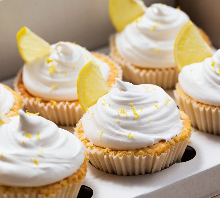Frontalsicht: Zitronen-Cupcakes mit süßem Hut in Muffin-Formen | © Shutterstock / Marharyta Kovalenko