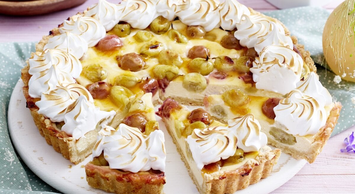 Auf einem Teller steht eine Stachelbeer-Baiser-Käsetarte. Sie ist mit Baisertuffs verziert.
