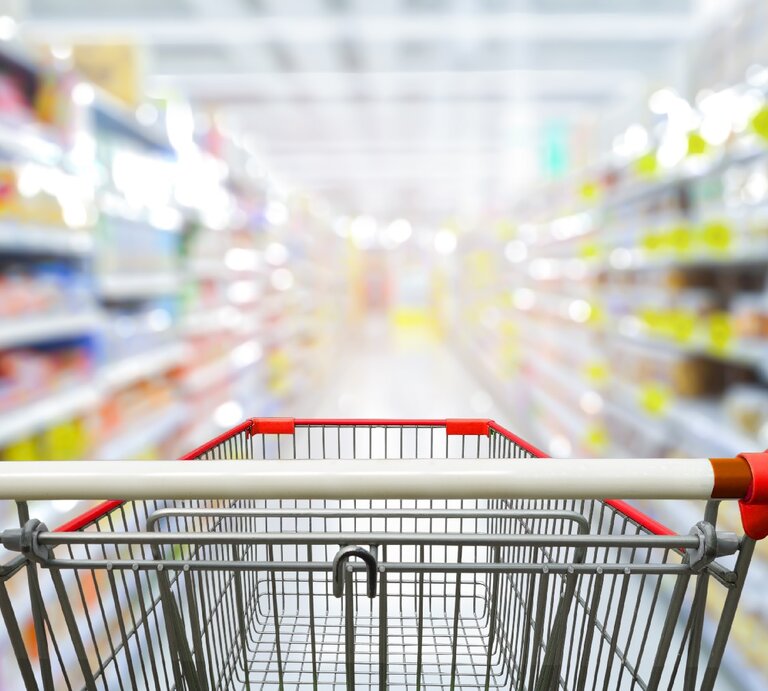 Ein leerer Einkaufswagen in einem Supermarktgang. Die Produkte sind unscharf zu erkennen. | © Shutterstock/ non c
