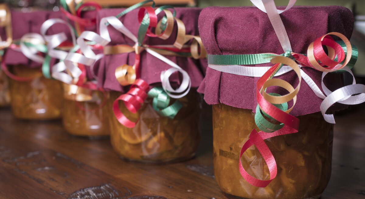 Selbst gemachte Marmeladen in Gläsern stehen mit Schleifen und lila Stoff auf dem Tisch.