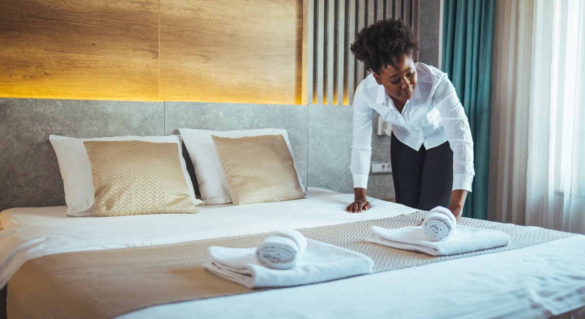 Eine Hotelangestellte streicht den Bezug eine Bettes glatt.