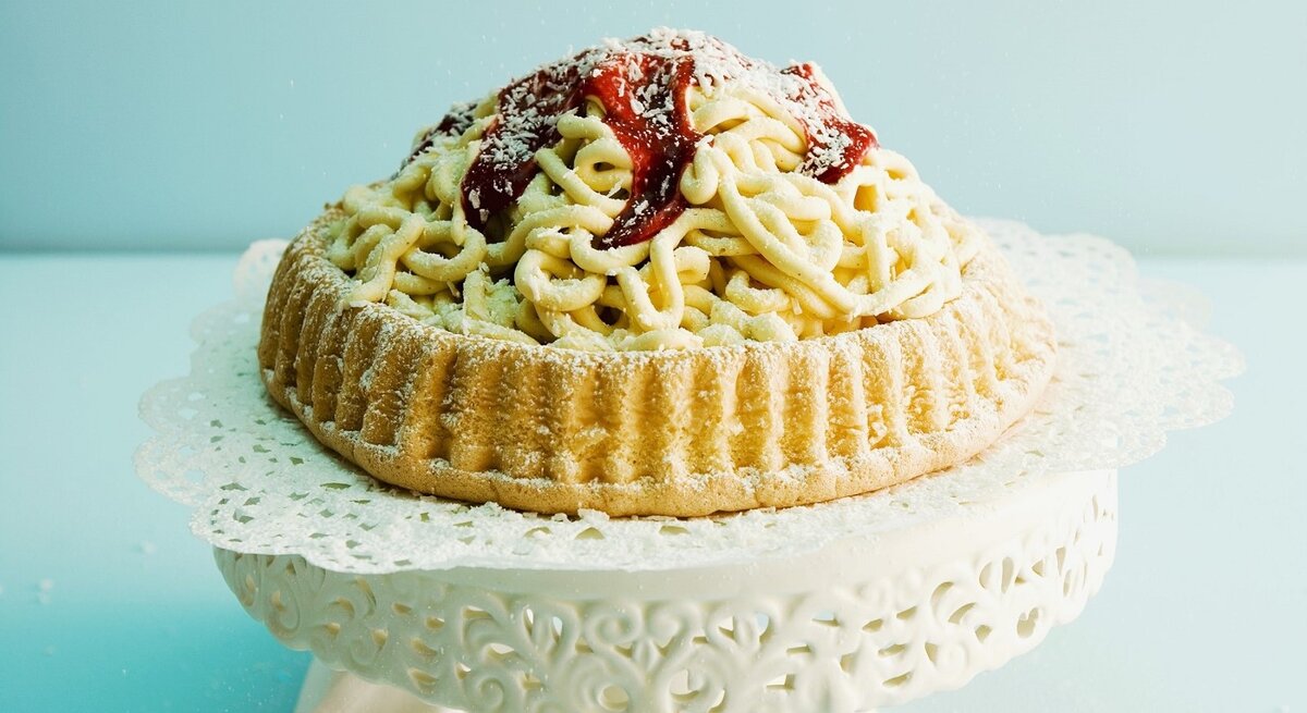 Auf einem Tortenteller steht eine Spaghettieistorte. Sie ist mit Johannisbeergelee und Puderzucker überzogen. 