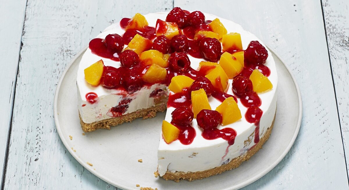 Auf einem Teller liegt ein Pfirsich-Melba-Käsekuchen. Er ist mit Himbeersoße überzogen. 