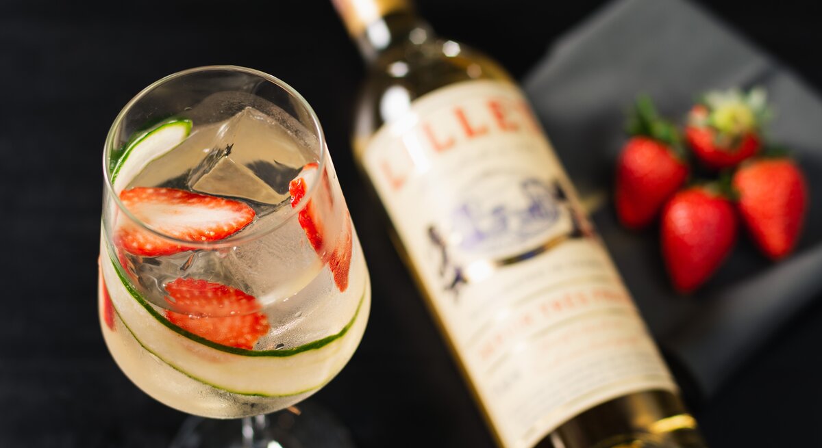 Lillet Gin Tonic in Weinglas mit Lillet-Flasche und Erdbeeren. Draufsicht.