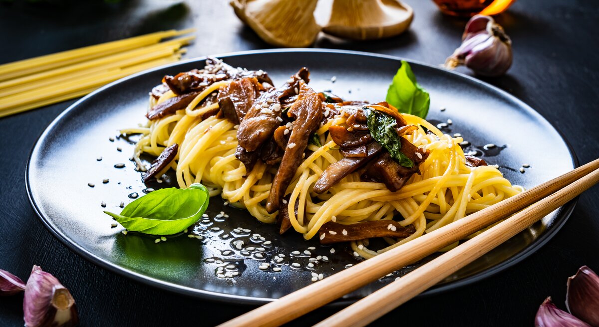 Ein schwarzer Teller mit Pasta mit Sojabutter und Pilzen neben frischen Zutaten