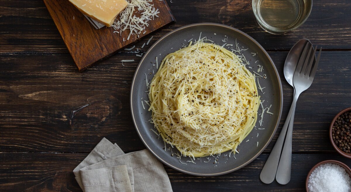 Spaghetti mit geriebenem Käse auf Holztisch.