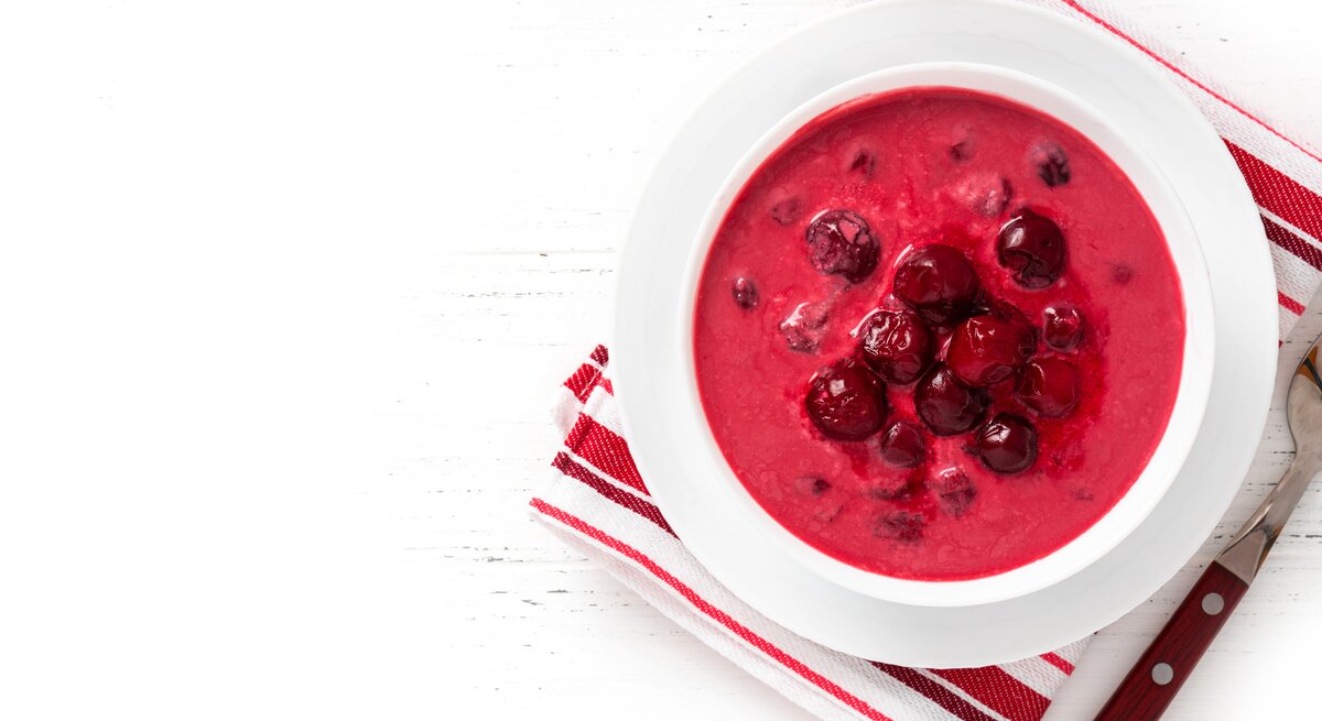 Ein weißer Teller mit der roten Suppe auf rot-weißem Tuch und weißem Tisch. Alles direkt von oben fotografiert.
