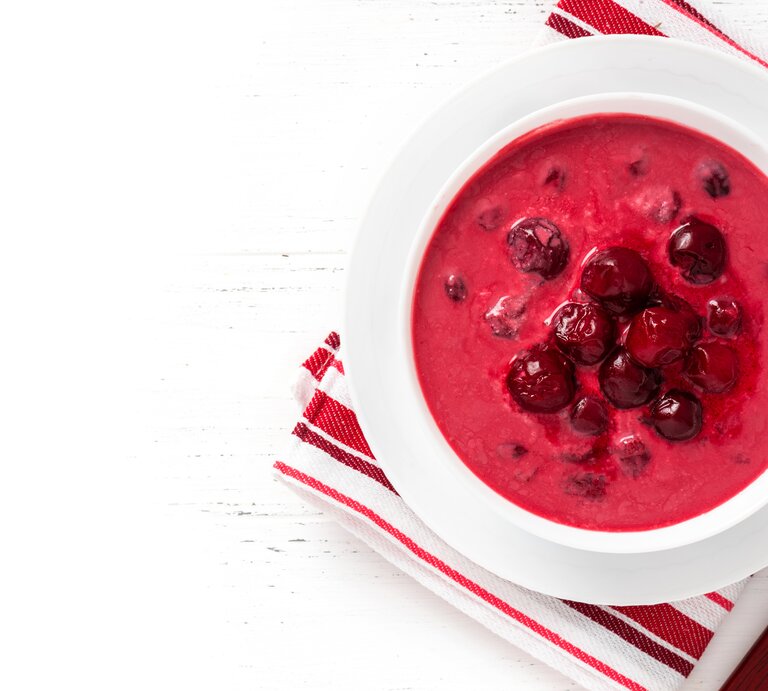 Ein weißer Teller mit der roten Suppe auf rot-weißem Tuch und weißem Tisch. Alles direkt von oben fotografiert. | © Getty Images/Svetlana Monyakova