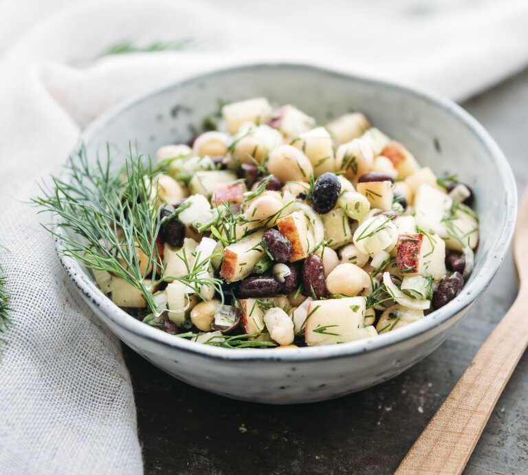 Eine Schüssel Apfel-Bohnensalat mit Kichererbsen und Dill, daneben ein Holzlöffel. | © Getty Images/ Westend61