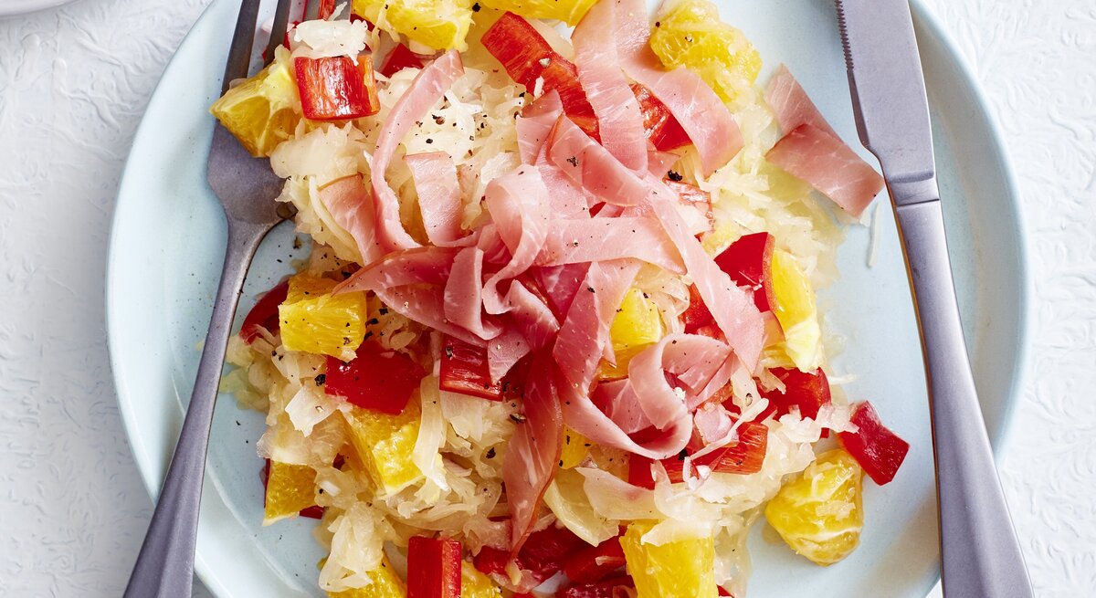 Sauerkrautsalat mit Orange und Schinken auf Teller angerichtet.