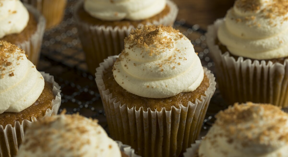 Ein paar Zimtschnecken-Cupcakes mit Creme-Haube auf einem Holzbrett.
