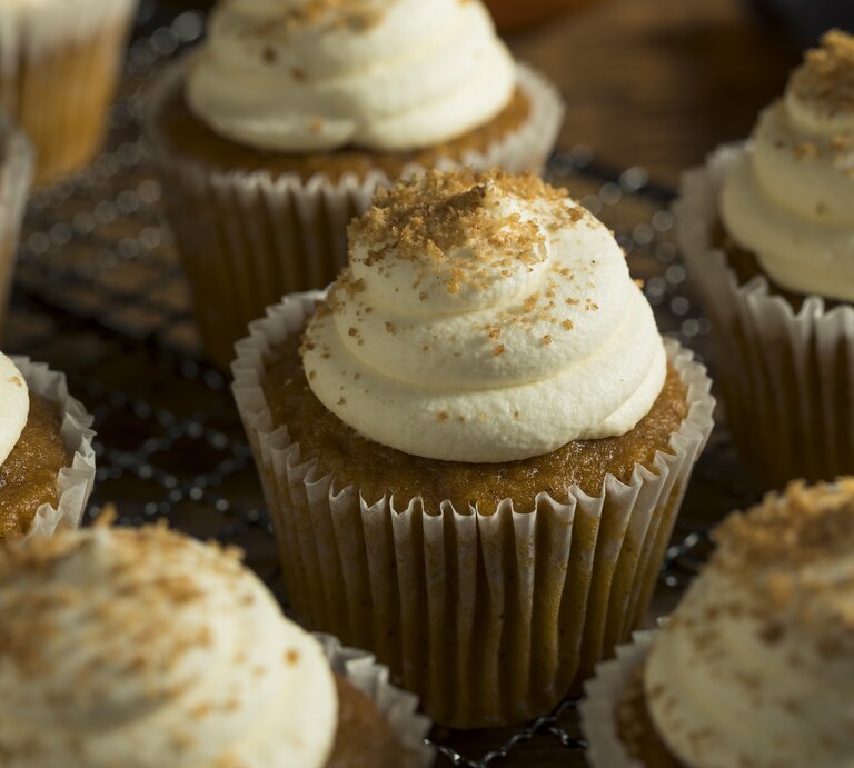Ein paar Zimtschnecken-Cupcakes mit Creme-Haube auf einem Holzbrett. | © Getty Images/ 	bhofack2