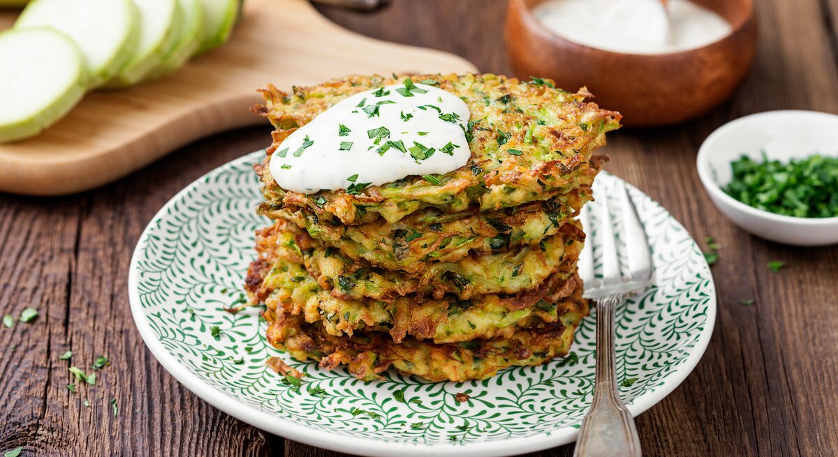 Ein Stapel Kartoffelpuffer mit Mangold und einem Klecks Quark auf einem Teller mit einer Gabel.