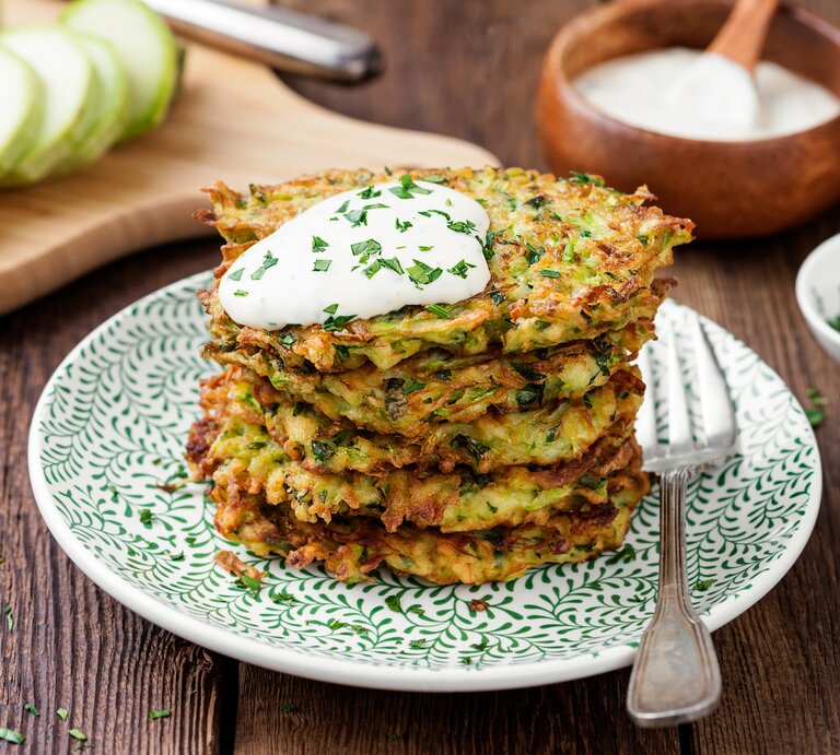 Ein Stapel Kartoffelpuffer mit Mangold und einem Klecks Quark auf einem Teller mit einer Gabel. | © Shutterstock/ nelea33
