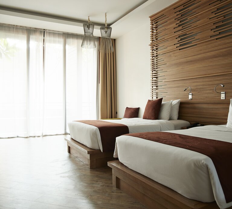 Modern gestaltetes Hotelzimmer mit zwei Einzelbetten. Jedes Bett ist mit einem weißen Laken und einem dunkelbraunen Bettschal am Fußende ausgestattet. | © Klaus Vedfelt / GettyImages