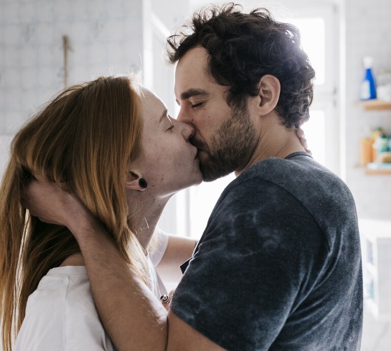 Ein junges Paar küsst sich innig in einem hellen Badezimmer, die Frau mit langen, roten Haaren, der Mann mit dunklen Locken. | © Willie B. Thomas via Getty Images