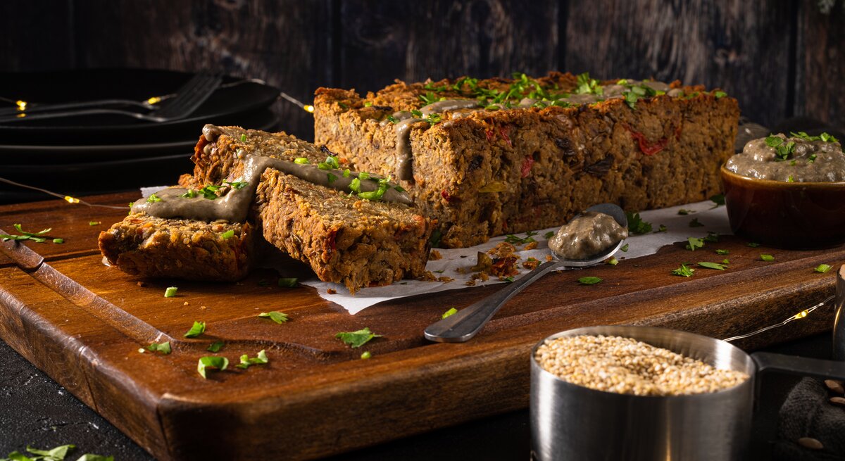 Auf einem großen Holzbrett liegt ein angeschnittener veganer Nussbraten mit etwas Soße beträufelt, drumherum eine Lichterkette und dunkler Hintergrund.
