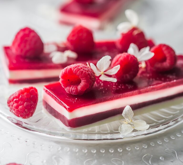 Panna-Cotta-Himbeer-Schnitten, garniert mit frischen Himbeeren und kandierten Früchten, serviert auf einem Kuchenteller auf hellem Untergrund.  | © StockFood/ PhotoCuisine