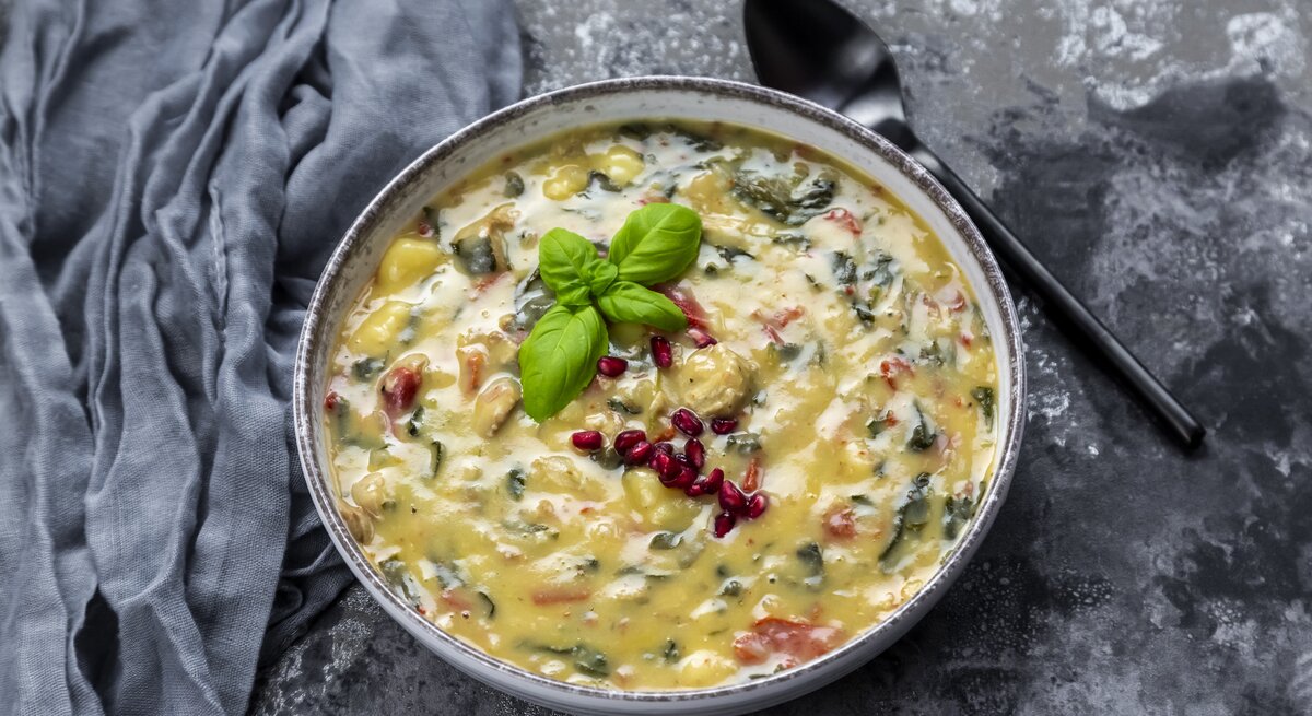 Eine Suppenschüssel mit Gnocchi-Spinat-Suppe auf grauem Hintergrund.
