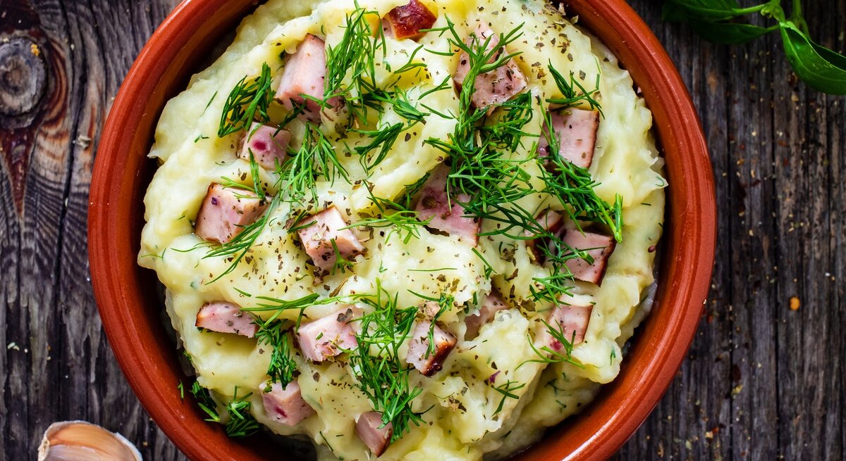 Dill-Kartoffelpüree mit Leberkäse in roter Schüssel auf dunklem Holz. 