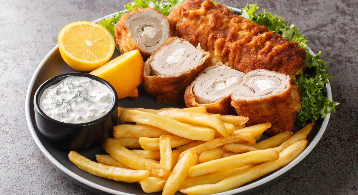 Serbisches Schnitzel mit Frischkäse-Füllung, dazu Pommes und Tatarsoße auf schwarzem Teller. 