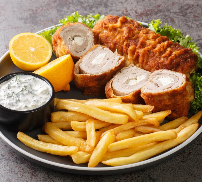 Serbisches Schnitzel mit Frischkäse-Füllung, dazu Pommes und Tatarsoße auf schwarzem Teller.  | © Getty Images/ALLEKO