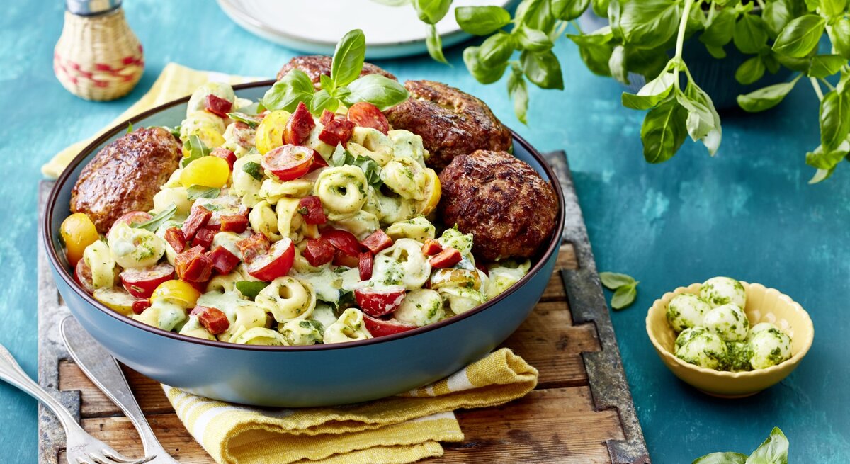 In einer Schüssel ist ein Tortellinisalat mit Hackbällchen angerichtet. Er ist mit Gemüse und Gewürzen verfeinert.