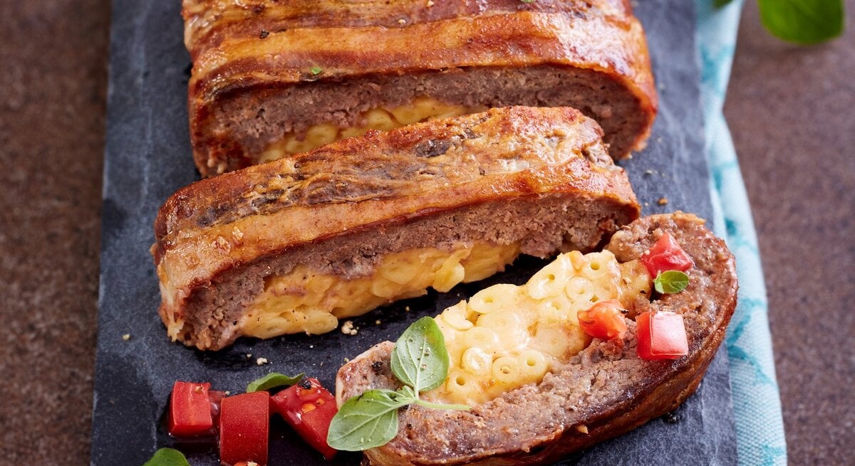 Auf einem Steinbrett ist ein Hackbraten mit Makkaroni-Füllung angerichtet. Er ist braun gebraten und sieht knackig aus.