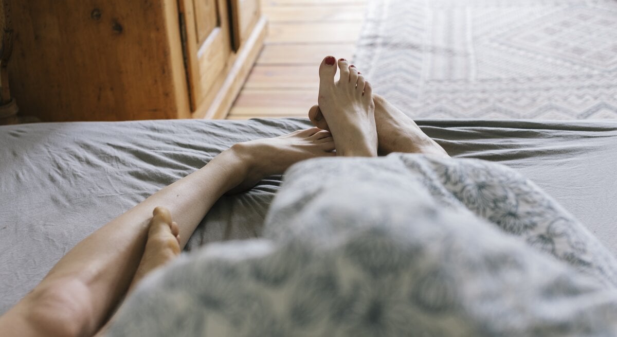 Füße von Mann und Frau im Bett zu sehen