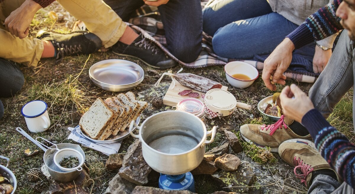 Eine Gruppe an Freunden frühstücken beim Camping-Ausflug.
