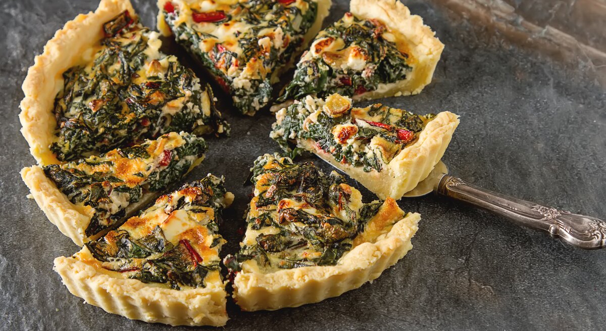Eine geschnittene vegane Mangold-Quiche mit Lauch auf dunklem Untergrund.