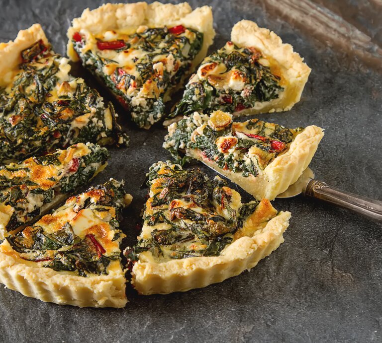 Eine geschnittene vegane Mangold-Quiche mit Lauch auf dunklem Untergrund. | © Shutterstock/ Gaus Alex