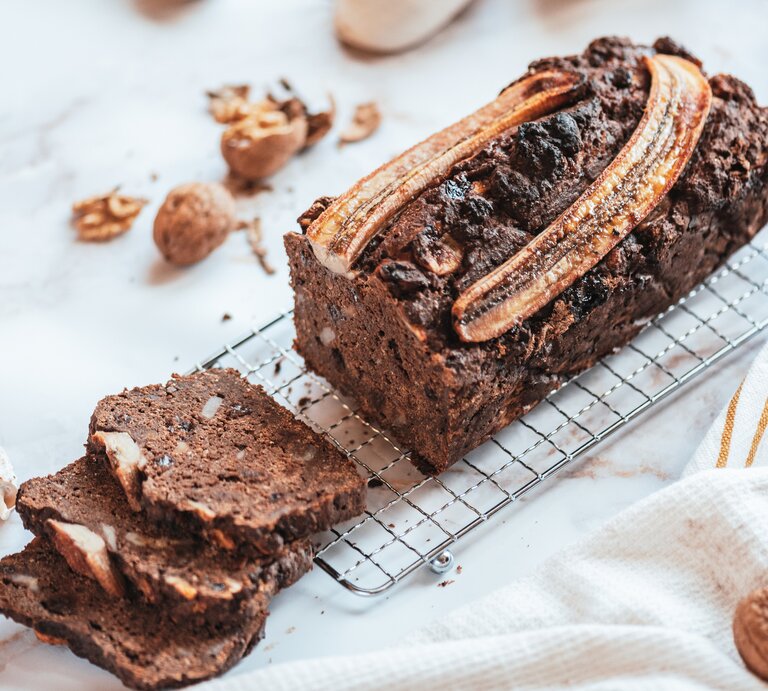 Ein angeschnittenes Schoko-Bananenbrot auf einem Kuchengitter, drumherum liegen geknackte Walnüsse. | © Getty Images/ Rocky89