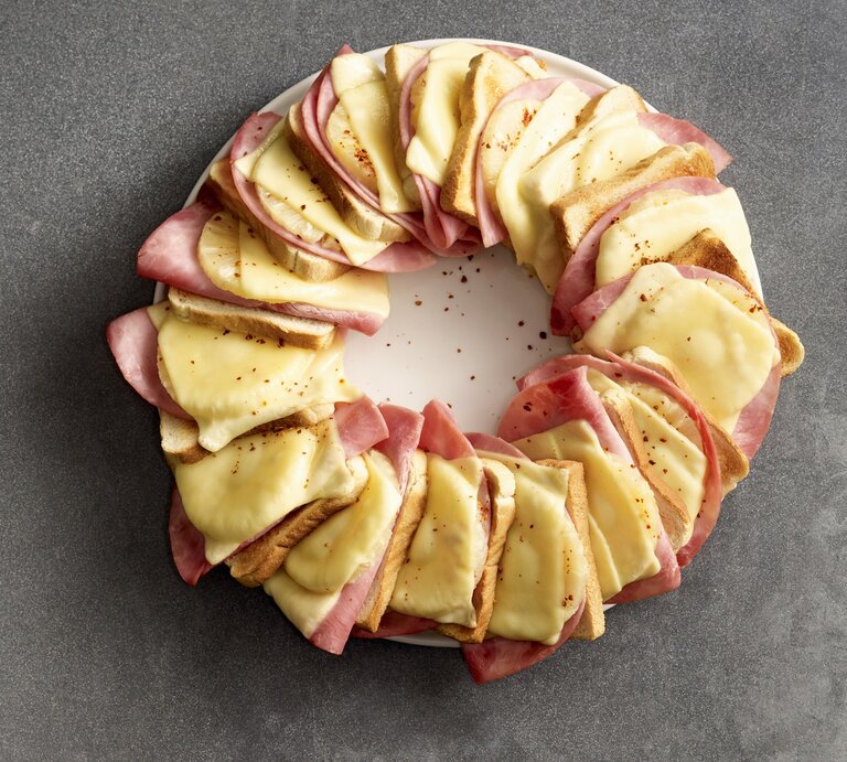 Hawaii-Toastbrot-Ring, bestehend aus abwechselnden Lagen von Gouda, Schinken, Ananas und Toastscheiben. In einem Ring aneinandergereit überbacken und mit Chiliflocken bestreut auf einem weißen Teller serviert.  | © Stockfood/Gräfe & Unzer Verlag / Lang, Coco