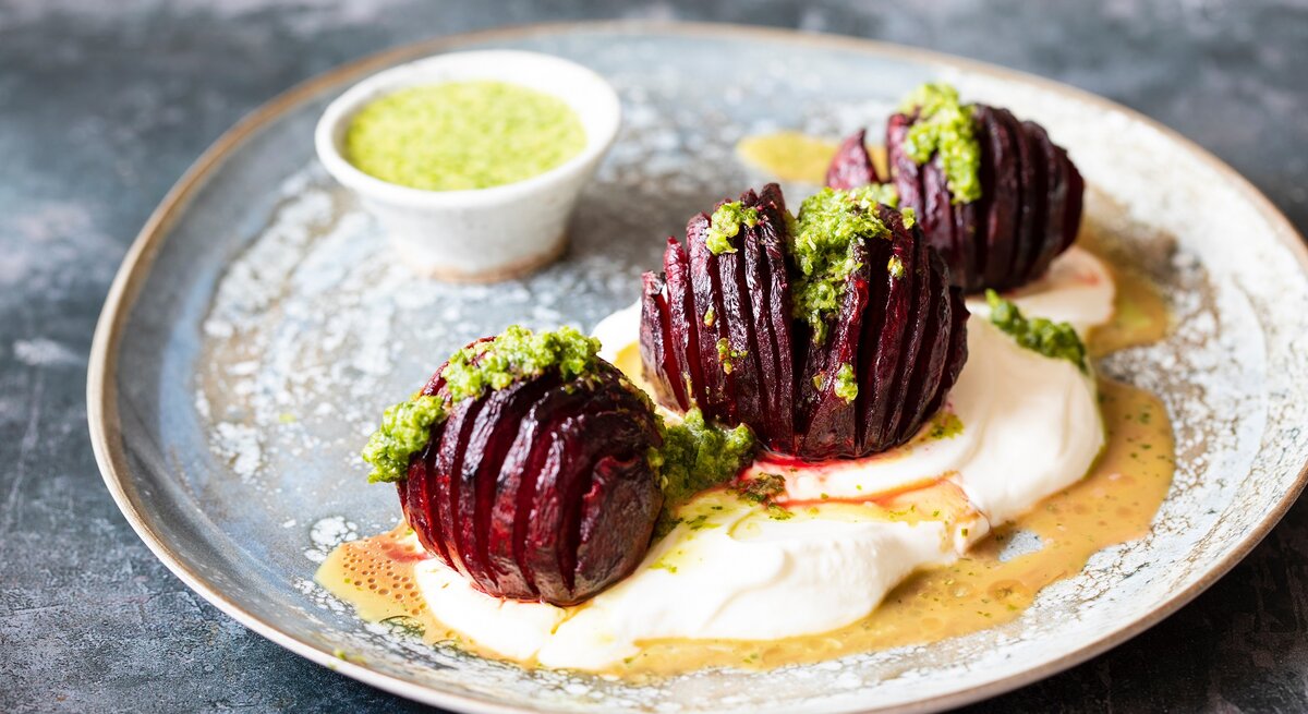 Ein Teller mit drei Hasselback-Beten, grünem Dressing und Joghurt.