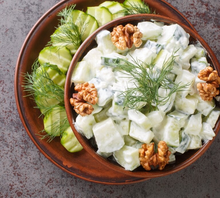 Bulgarischer Gurkensalat mit frischem Dill, Joghurt und ganzen Walnüssen, serviert in einer dunklen Keramikschale auf steinernem Untergrund.  | © Getty Images /  ALLEKO