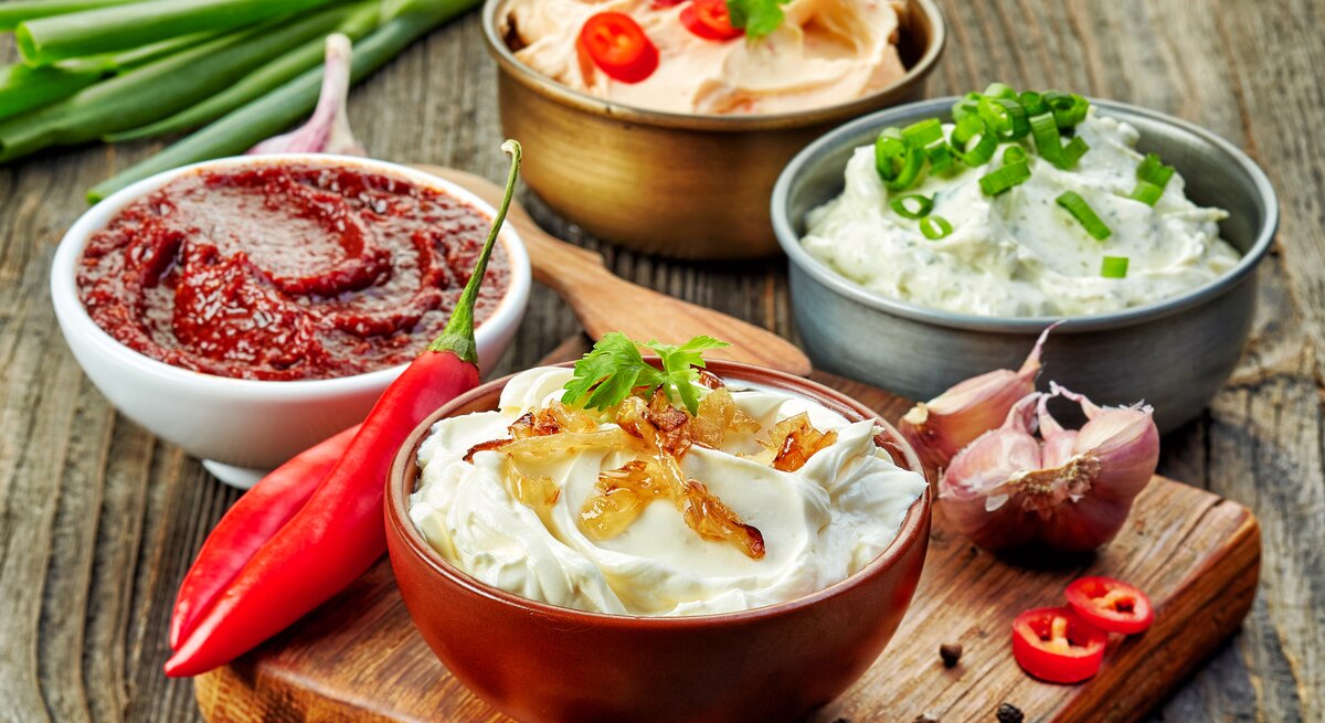 Verschiedene Dips in unterschiedlichen Schüsseln auf einem Holztisch.