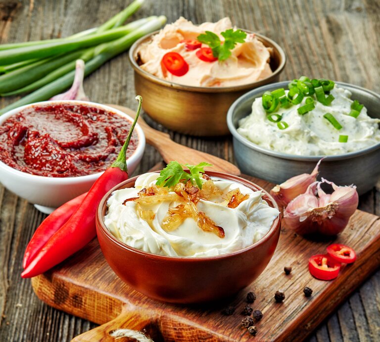 Verschiedene Dips in unterschiedlichen Schüsseln auf einem Holztisch. | © iStock/Magone