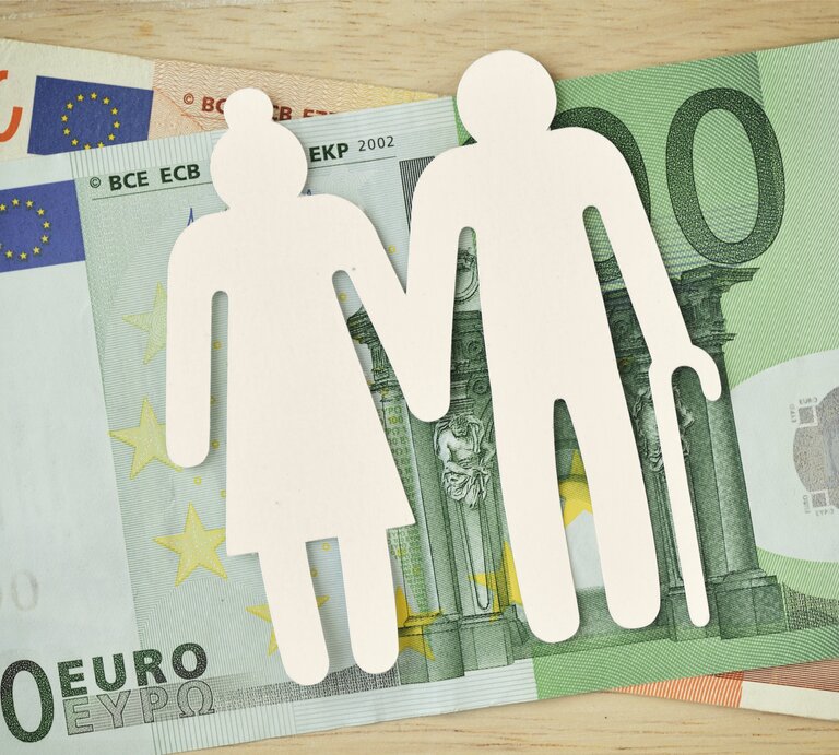 Ein Seniorenpaar aus Papier liegt auf Euro-Geldscheinen. | © Getty Images / Luisella Sem / EyeEm
