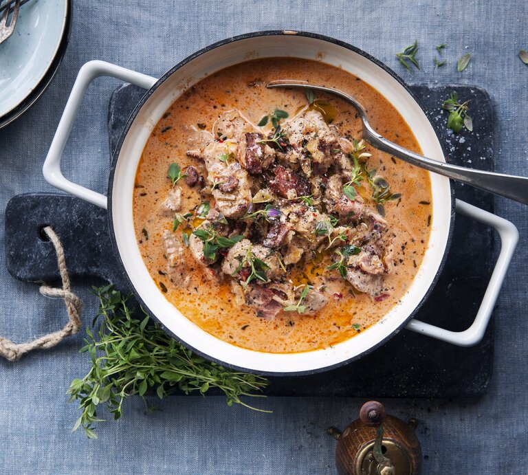 Eintopf mit Schweinefilet und getrockneten Tomaten, garniert mit frischem Thymian und angerichtet mit Sahne in einem großen Topf auf einer Schierferplatte.  | © StockFood / Hilden Smith, Eva