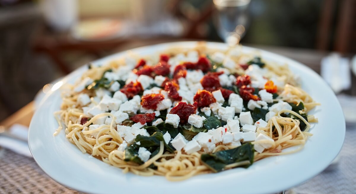Spaghetti mit Spinat, Feta und getrockneten Tomaten auf weißem Teller. 