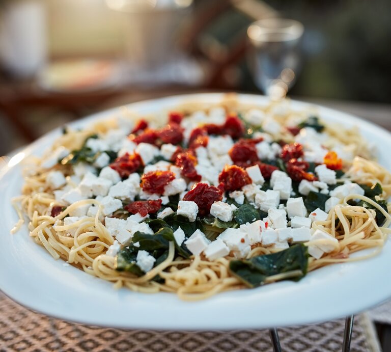 Spaghetti mit Spinat, Feta und getrockneten Tomaten auf weißem Teller.  | © Getty Images/LumiNola