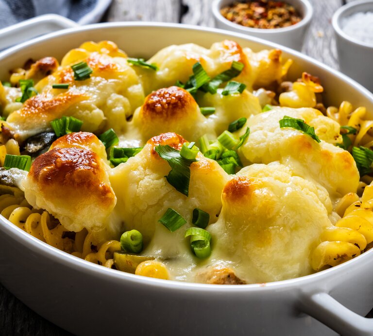 Schräg oben: ein überbackenes Blumenkohl-Gratin mit Hackfleisch und Käse in einer weißen Auflaufform steht auf einem Holztisch. | © © Shutterstock / Jacek Chabraszewski