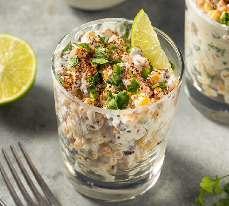 Zwei Gläser mit dem Salat auf einem grauen Untergrund. Daneben eine Limettenhälfte und ein paar Korianderzweige.  | © Shutterstock/ Brent Hofacker