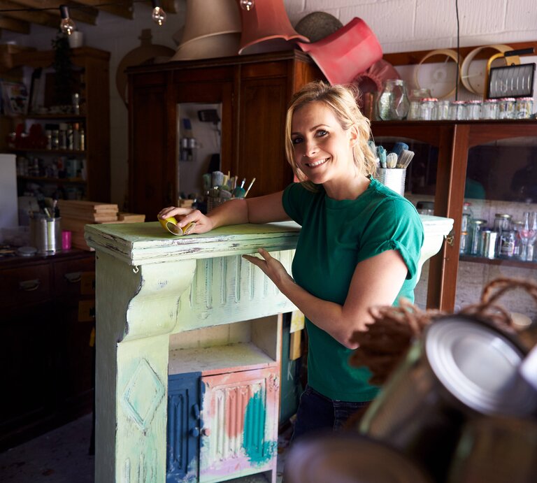 Upcycling: Eine Frau bearbeitet einen kleinen, alten Schrank. | © IMAGO / Shotshop