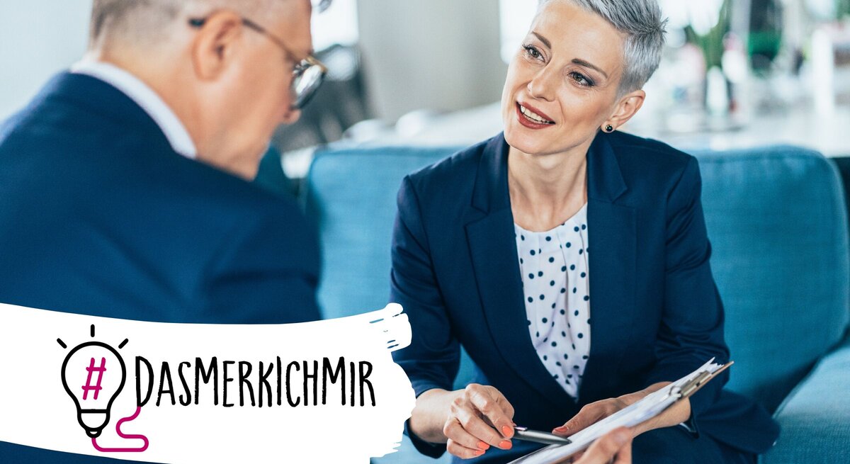 Das Bild zeigt ein professionelles Treffen zwischen einer Frau mit kurzen grauen Haaren und einem Mann, der von hinten zu sehen ist. Die Frau, die lächelnd und aufmerksam wirkt, trägt einen dunkelblauen Business-Anzug und ein gepunktetes Hemd. Sie hält einen Klemmbrett und scheint aktiv an dem Gespräch teilzunehmen oder dem Mann etwas zu erklären. Der Mann trägt einen dunklen Anzug und eine Brille. Im Vordergrund ist der Hashtag "#DAS MERK ICH MIR" neben einer Grafik einer Glühbirne zu sehen,