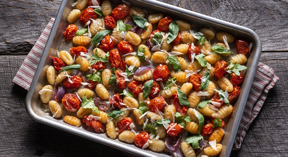 Gnocchi vom Blech mit italienischem Gemüse auf grauem Holz. 
