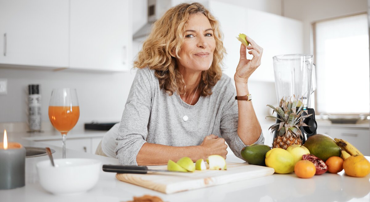 Frau mit geschältem Obst und Standmixer in einer Küche