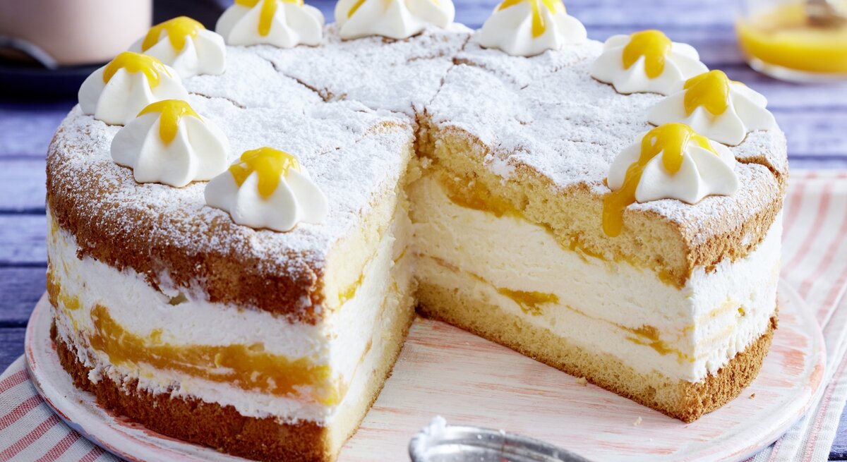 Auf einem Holzteller steht eine Quark-Mangotorte. Sie ist mit Puderzucker und Sahnetuffs verziert.